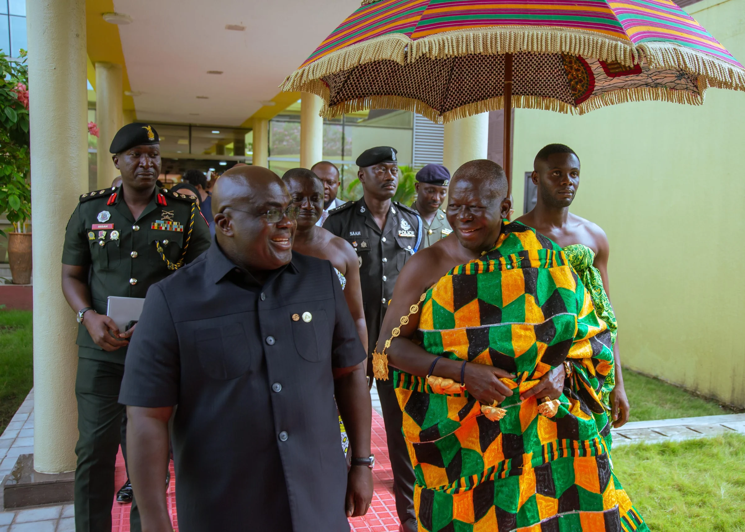 Julius Debrah walking beside a traditional ruler in kente, beneath a ceremonial umbrella